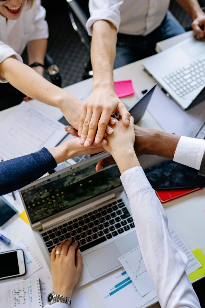 pexels photo 7793687 7793687 A diverse group of professionals stacking hands over a table symbolizing teamwork and collaboration.